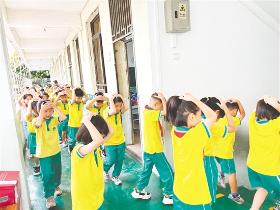 演練中，學(xué)生雙手抱頭、緊貼墻角，按照指定的逃生路線快速有序地撤離至操場(chǎng)安全區(qū)域。